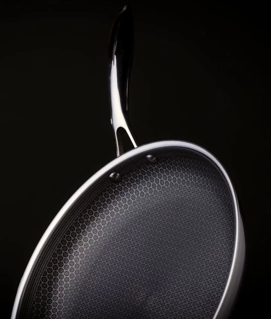 Close-up of a stainless steel frying pan against a black background.