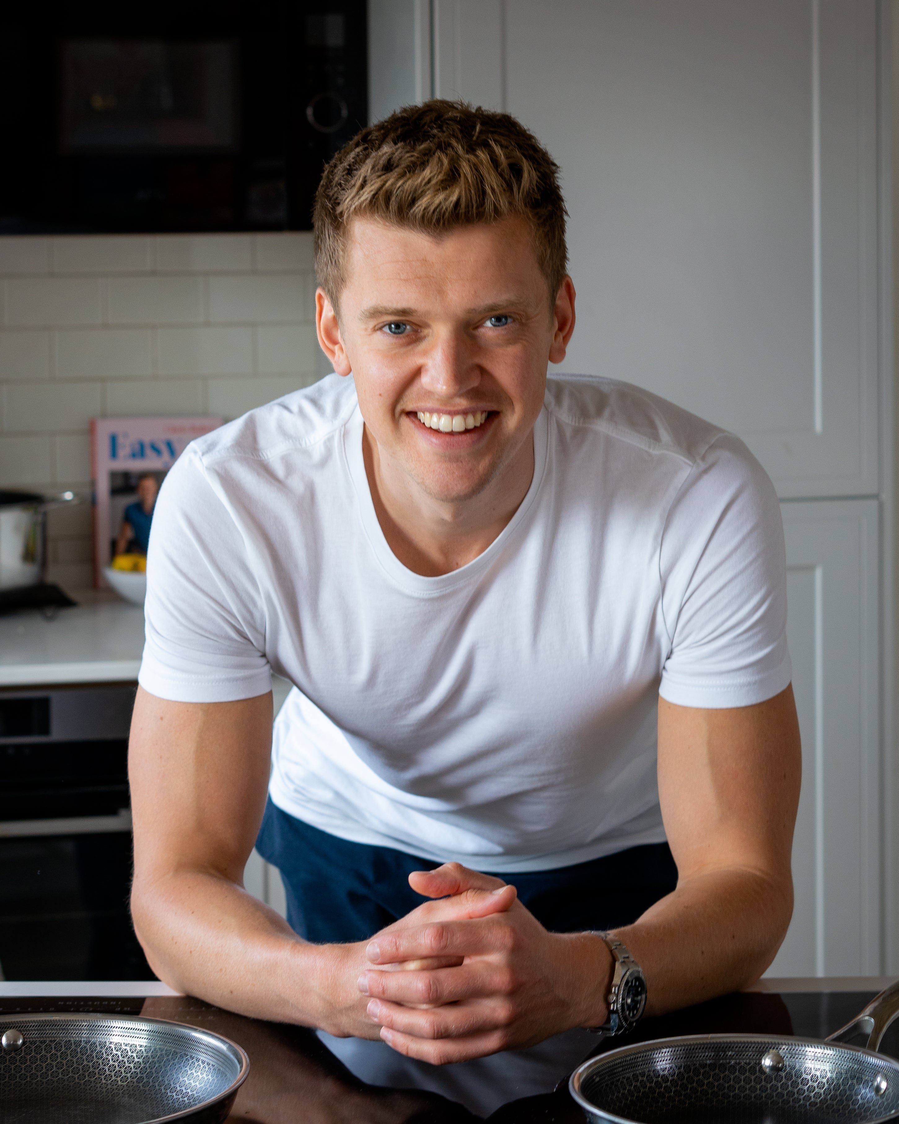 Man smiling in a kitchen with pans on a counter.